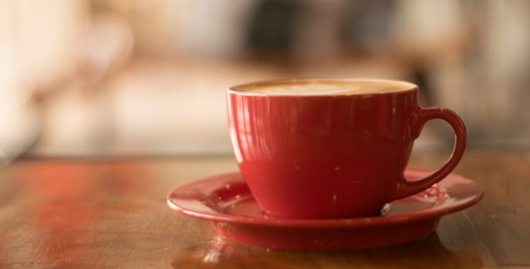 Coffee in a red ceramic cup with a saucer on a wooden table.